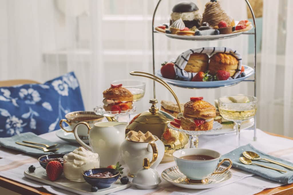 Afternoon tea for two with warm scones in a napkin-lined basket on a tiered stand, and cream and jam in small bowls