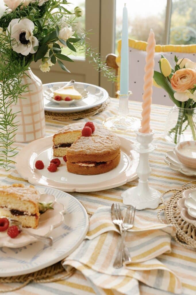 Striped linen tablecloth and napkin with scalloped plates holding a lemon tart slice and a jam sponge with raspberries