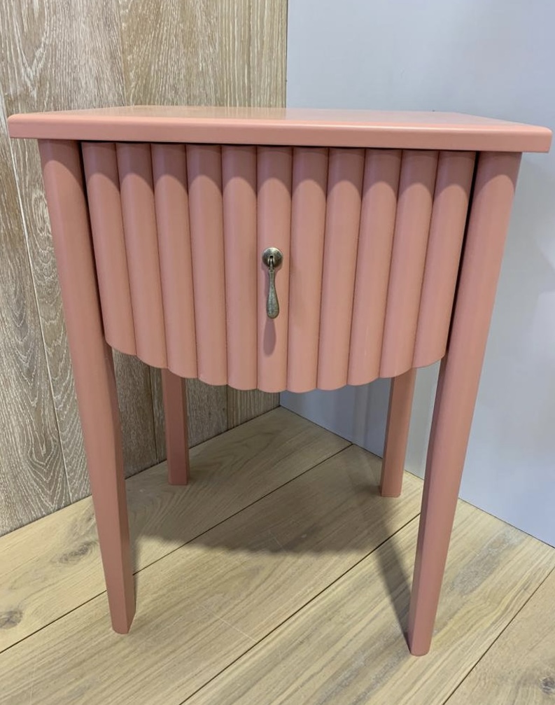 Pink fluted bedside table with curved front and tapered legs, ideal as a playful yet elegant accent in a pink and green bedroom.