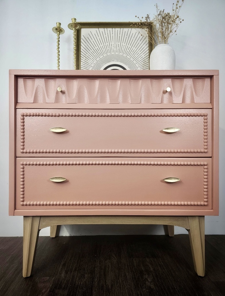 Pink chest of drawers with bobbin detailing and brass handles, styled with decorative accessories—ideal for adding character to a pink and green bedroom.
