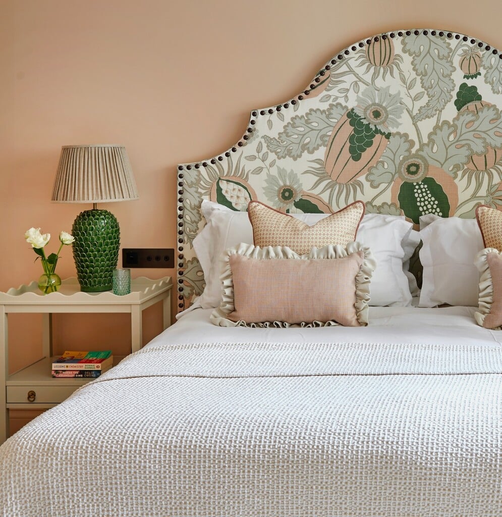 Dusky pink and green bedroom with Farrow & Ball Setting Plaster walls, a botanical upholstered headboard, ruffled pink cushions and a green glazed table lamp