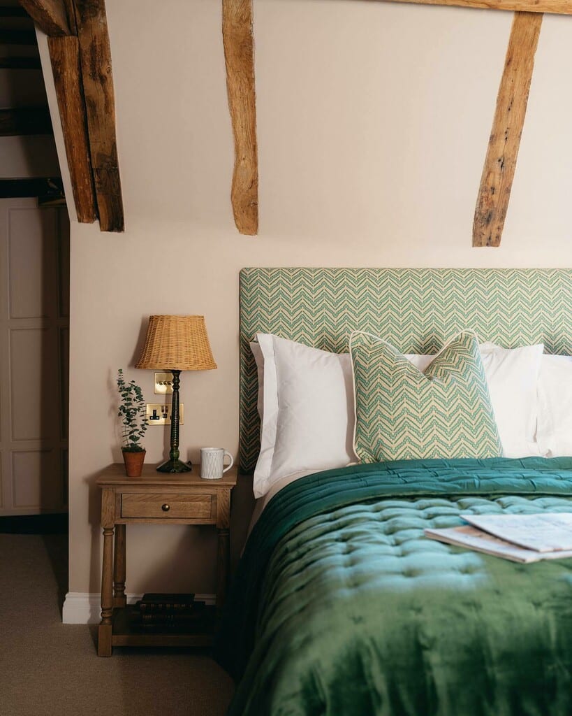Cottage bedroom with Farrow & Ball Setting Plaster walls, exposed oak beams, a green chevron headboard and a deep green quilted velvet bedspread