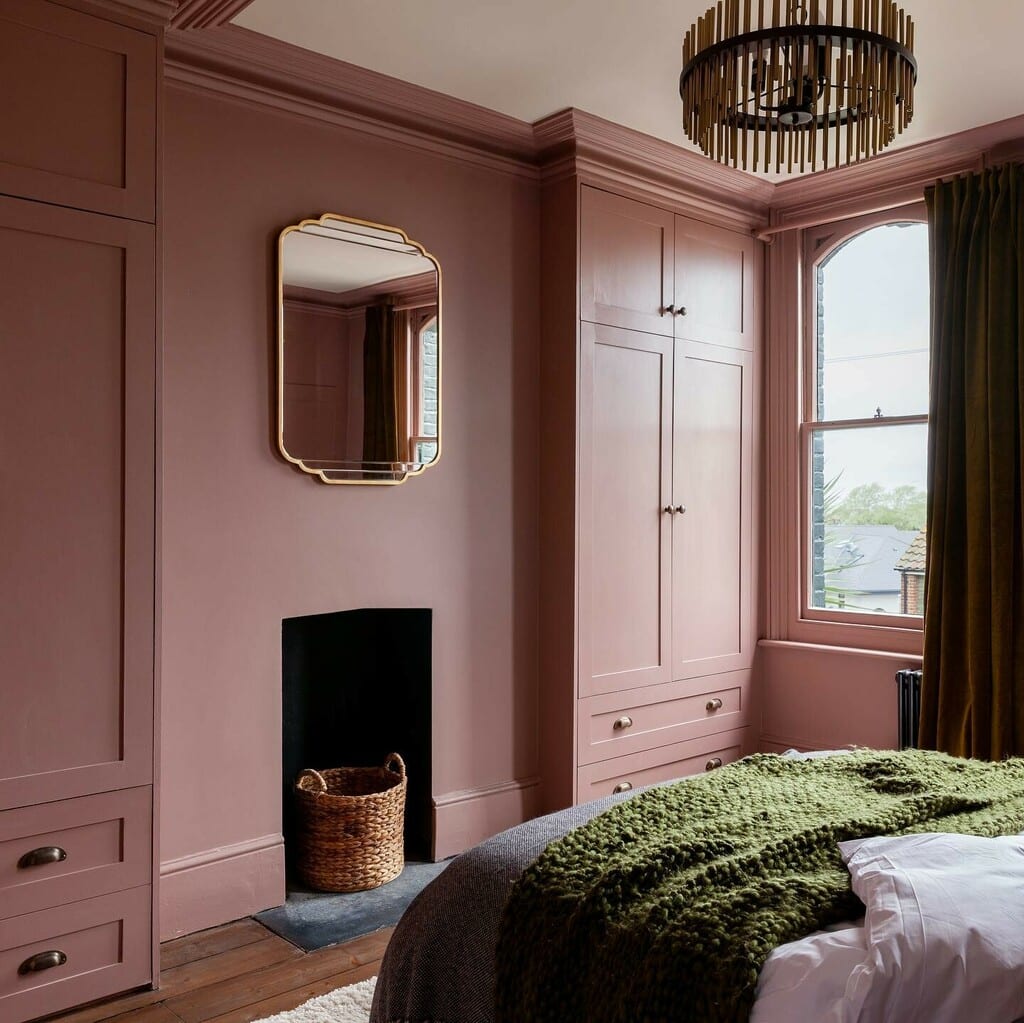 Sulking Room Pink bedroom with fitted wardrobes, smoky rose walls, dark flooring and a deep green knitted throw on the bed
