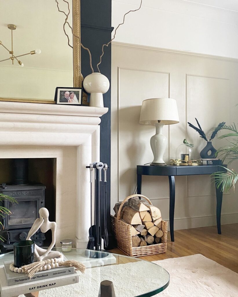 Black console table with cabriole legs in a living room beside a fireplace, styled with a large globe lamp and dried botanicals in a black vase, walls in Farrow & Ball Oxford Stone