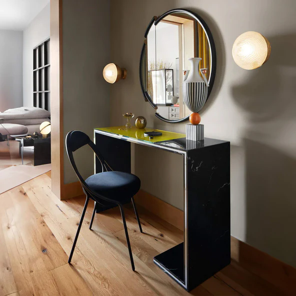 Black marble console table with slim cross-frame legs styled with a dome lamp, art books and a raw mineral sculpture against a warm stone wall