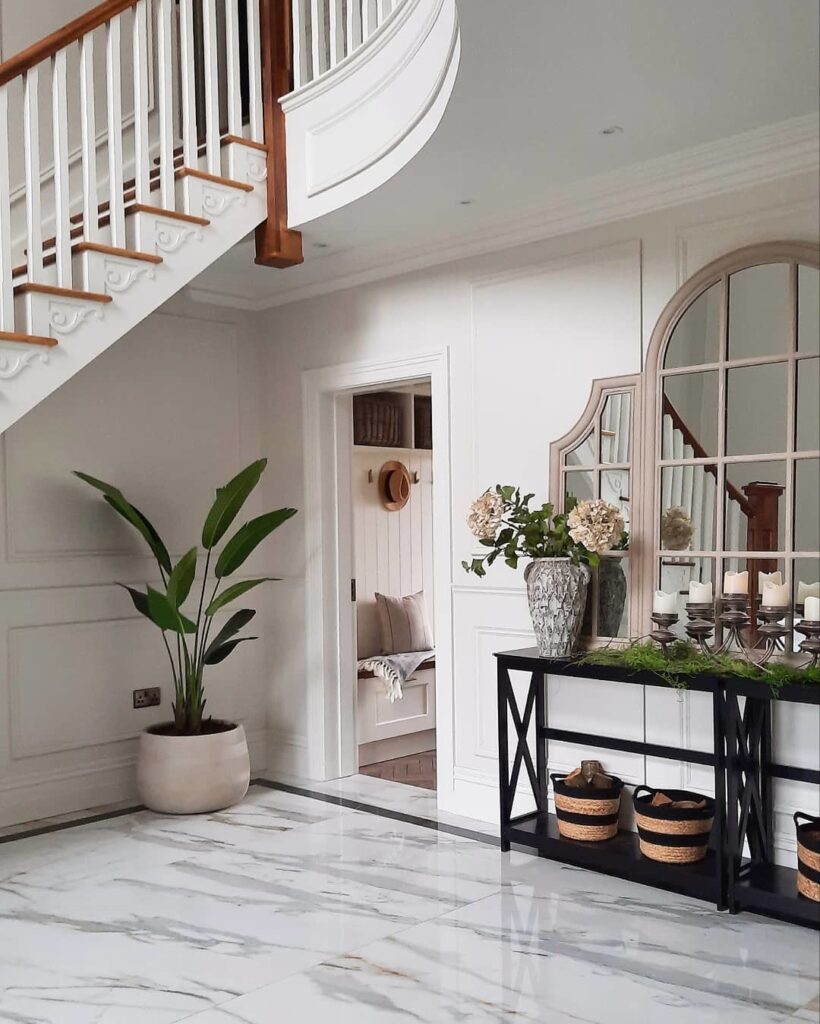 Black X-frame console table in a grand white hallway styled with a large arched mirror and wicker baskets underneath, walls in Farrow & Ball Strong White