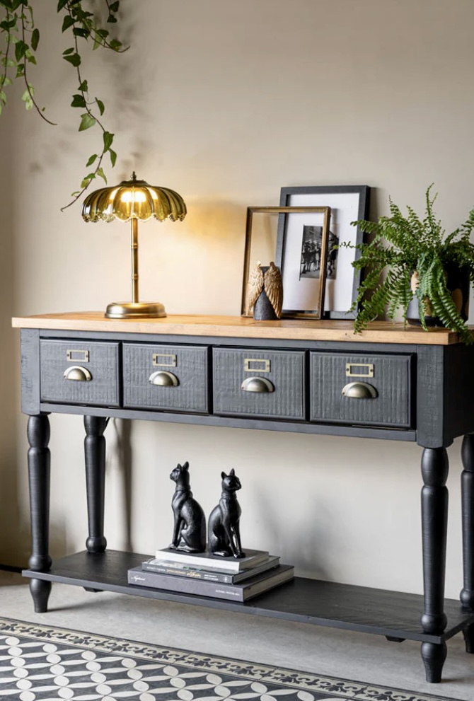 Modern black console table styled with gold lamp, black cat bookends, and trailing greenery