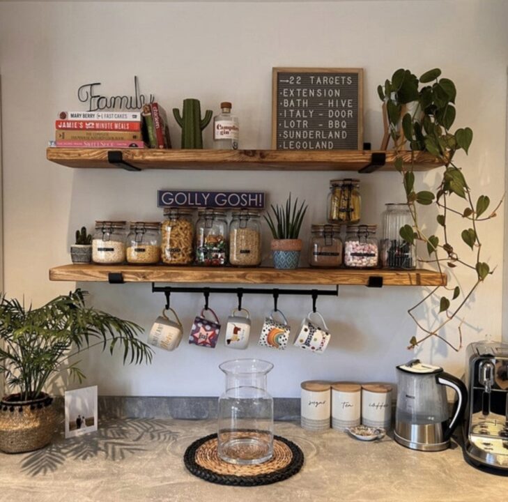 Rustic kitchen floating shelves made from reclaimed wood, styled with glass jars, cookbooks, and hanging mugs. The open shelving adds warmth and practicality, creating a cosy and organised kitchen space.