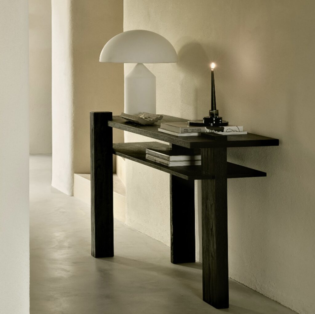 Modern black console table styled with sculptural decor including a mushroom lamp, candle, and books in a minimalist hallway