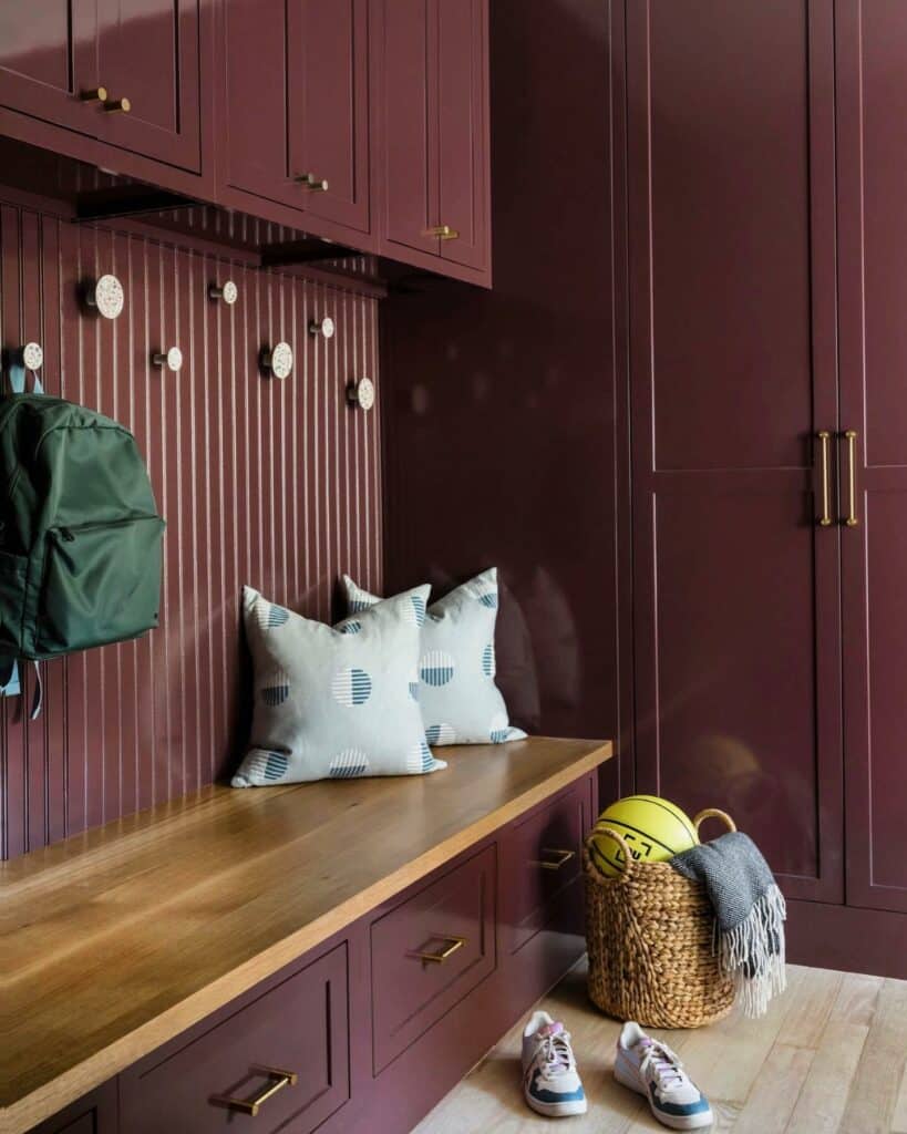 Hallway utility room with ribbed wood wall panelling in Farrow & Ball Brinjal, matching cabinetry, oak bench and brass hardware.