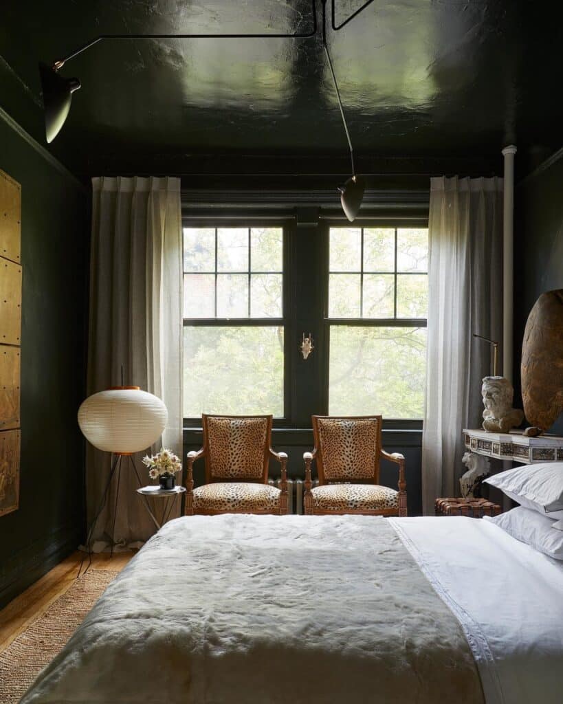 pair of leopard print accent chairs at the foot of a bed in a dark green bedroom with Studio Green walls and ceiling