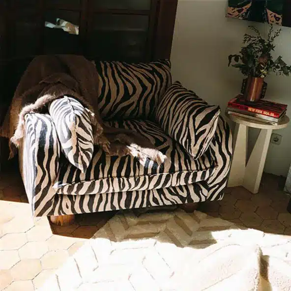 Dusty Deco Miles zebra print loveseat in a moody eclectic room with plant and side table