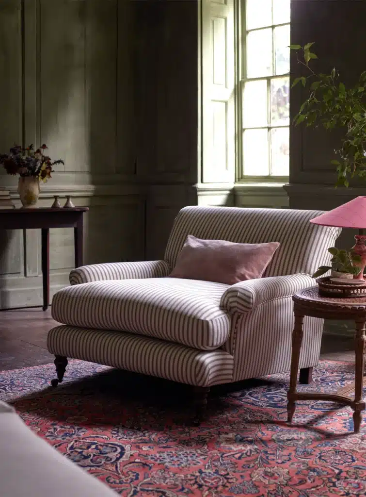 Sage green ticking stripe armchair in a dark panelled room with Persian rug