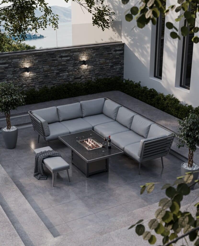 Garden corner sofa set with fire pit table and bench on grey stone patio with wall lights.