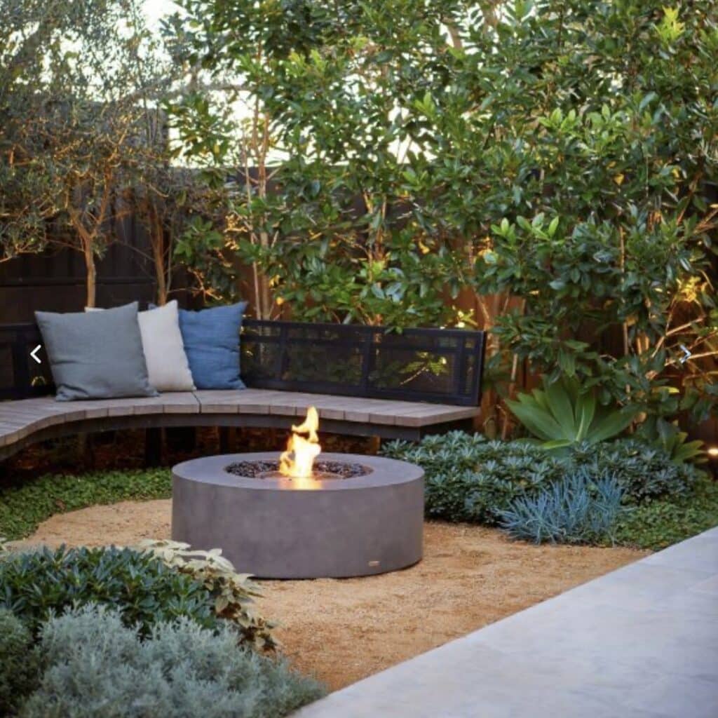 Curved corner seating arranged around a round outdoor fire pit in a planted garden