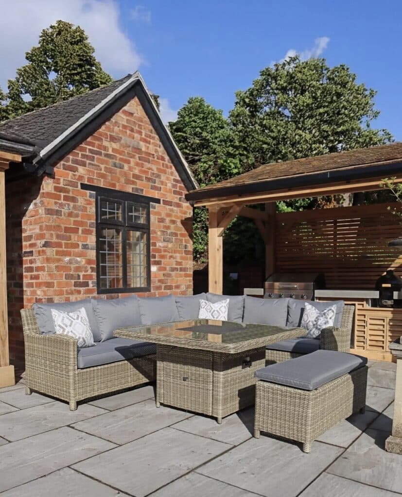 Corner garden sofa dining set with rattan-style square fire-pit table and bench on stone patio.