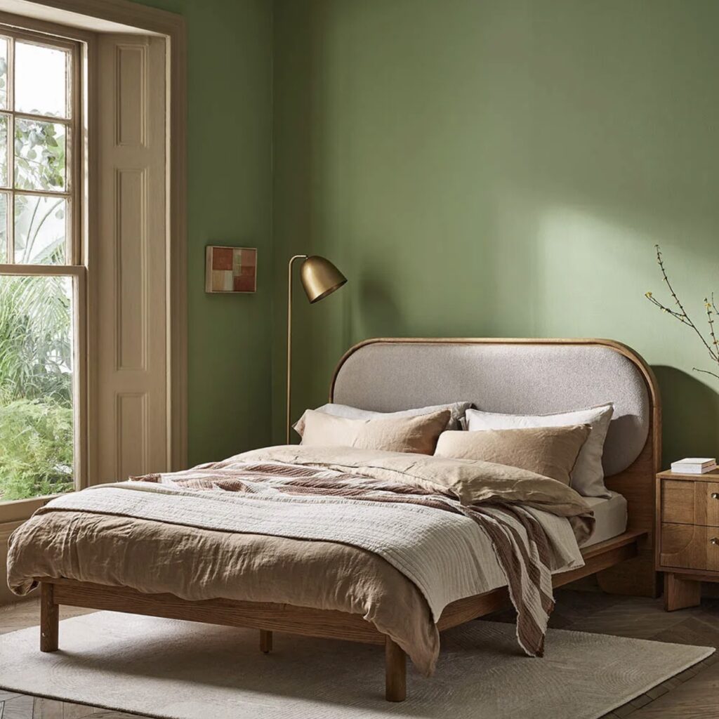 Green and beige bedroom with wooden bed frame, soft neutral bedding, and green painted walls