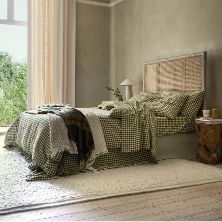 A serene green and beige bedroom featuring a rattan headboard, gingham bedding, and layered throws, creating a cosy and nature-inspired retreat.
