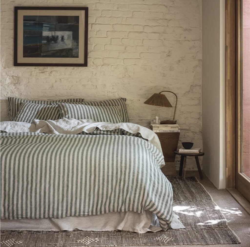 Striped green and beige bedding is the feature in this rustic beige and green bedroom, with wooden accents and rattan table lamp