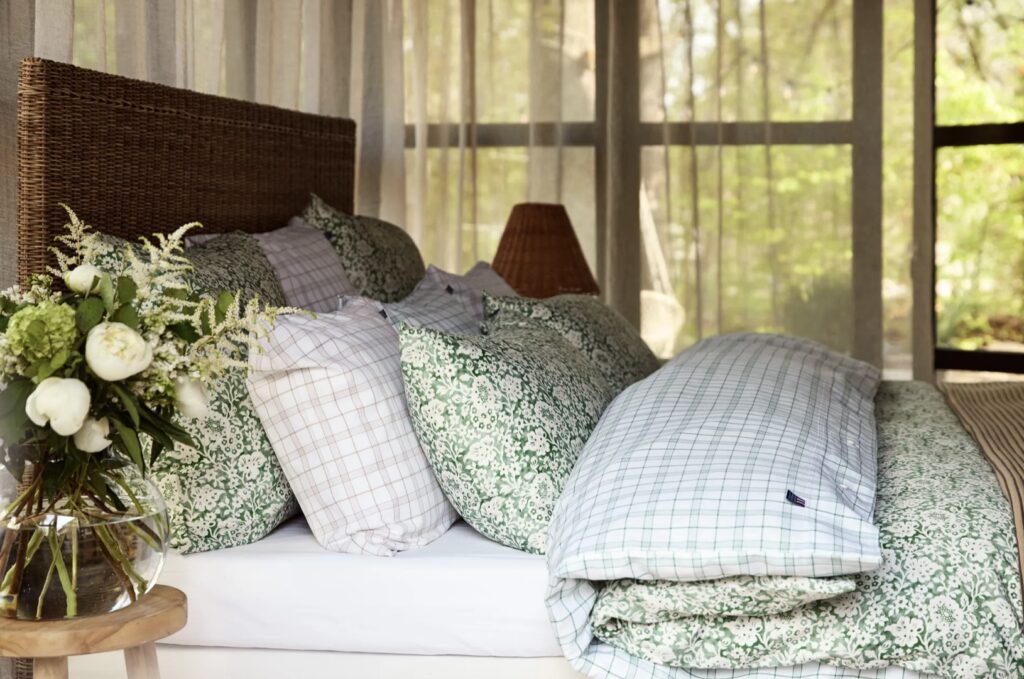Green floral bedding paired with beige accents, a rattan headboard, and a cosy plaid throw in a tranquil bedroom setting.