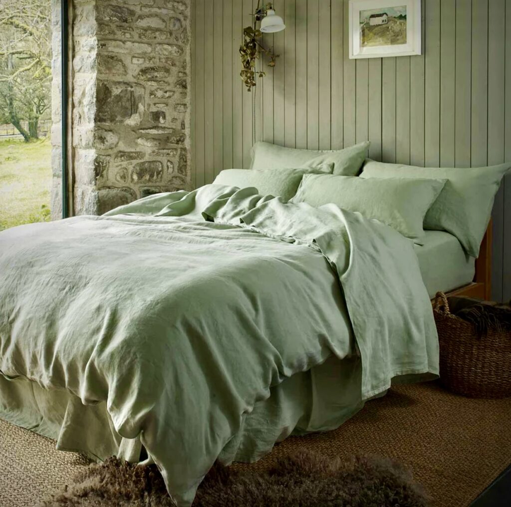 Green and beige bedroom with sage green linen bedding, a stone accent wall, and rustic decor elements.