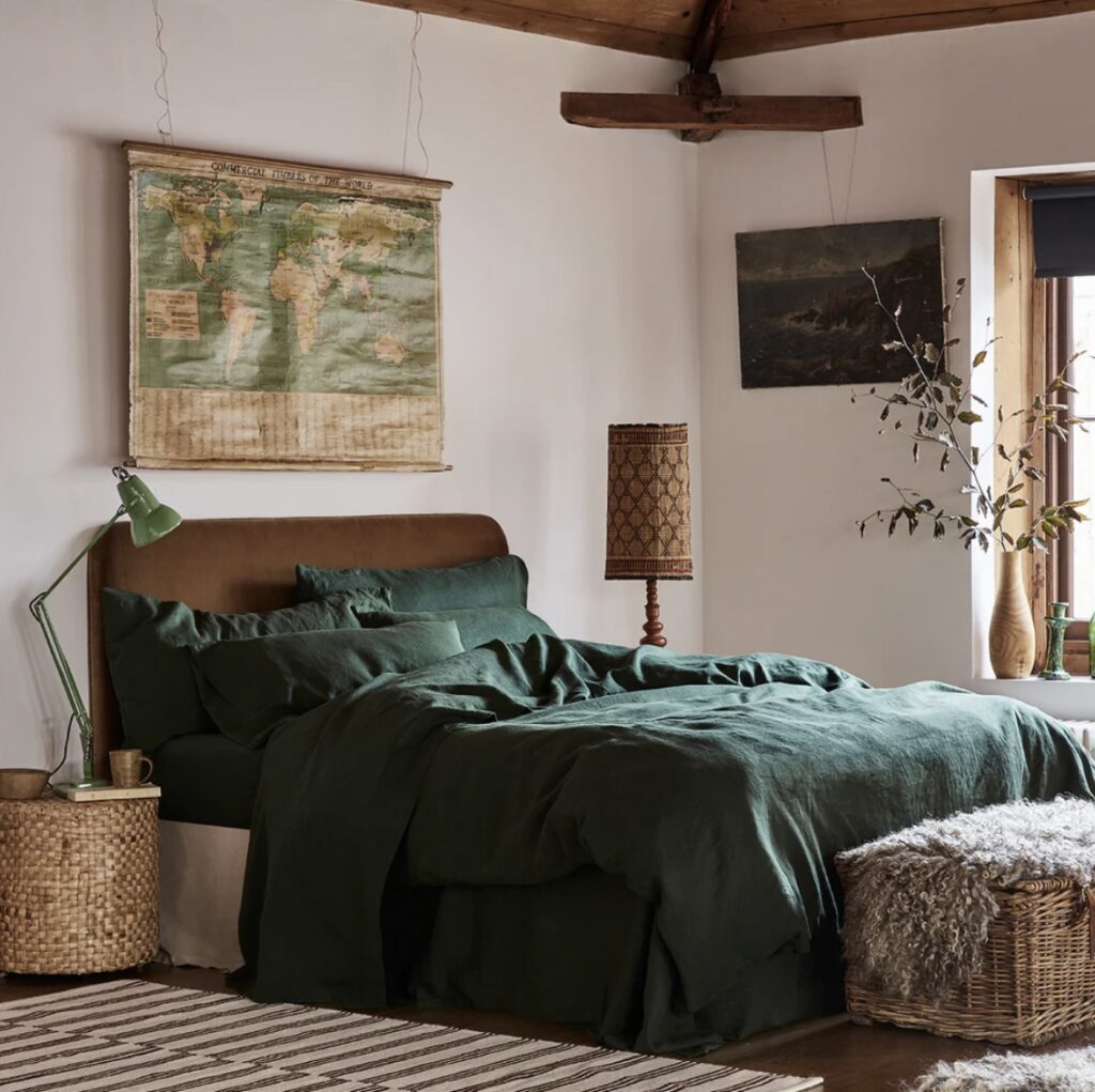 Green and beige bedroom featuring a fern green linen duvet cover, leather headboard, wicker accents, and vintage decor elements.