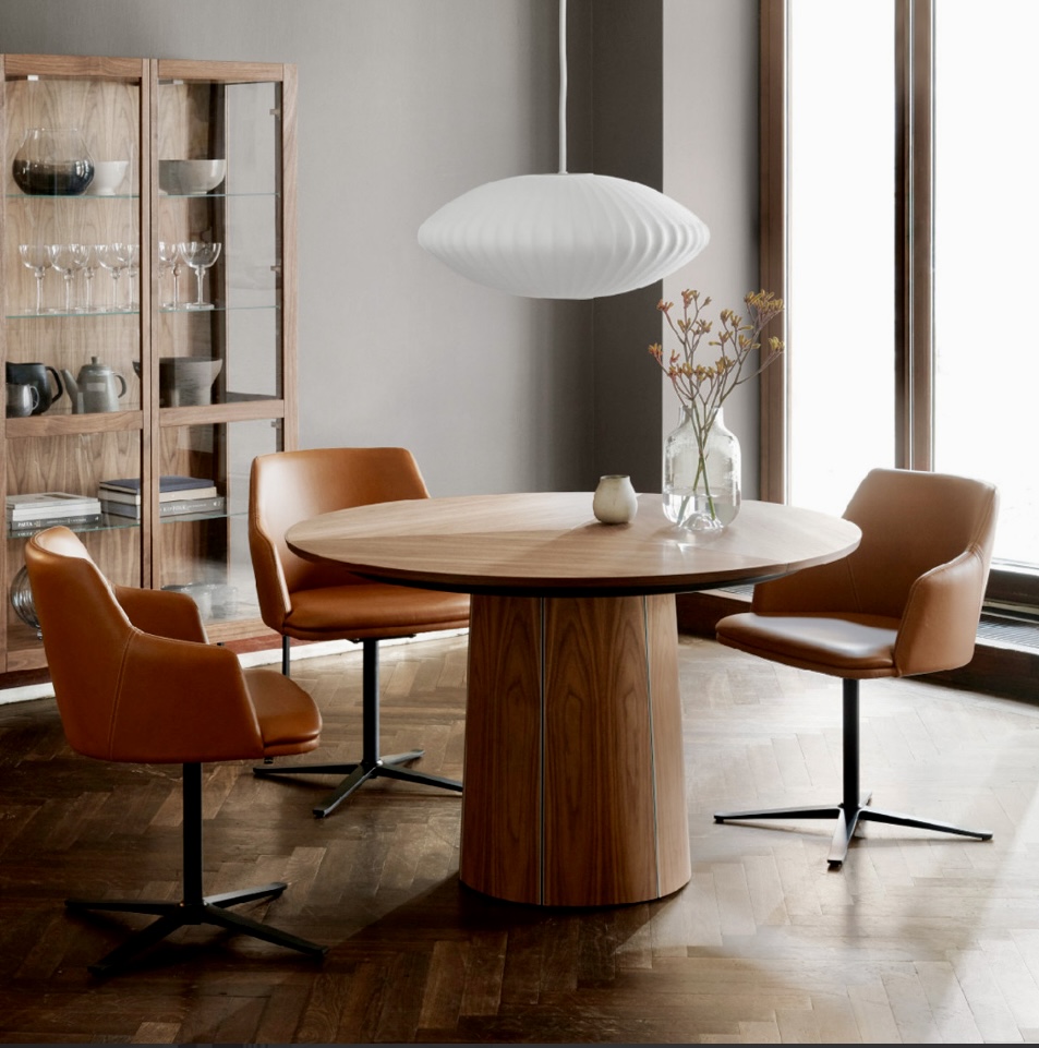 Contemporary round dining table in walnut finish, paired with tan swivel chairs in a modern interior, showcasing a round extendable dining table perfect for stylish urban living.