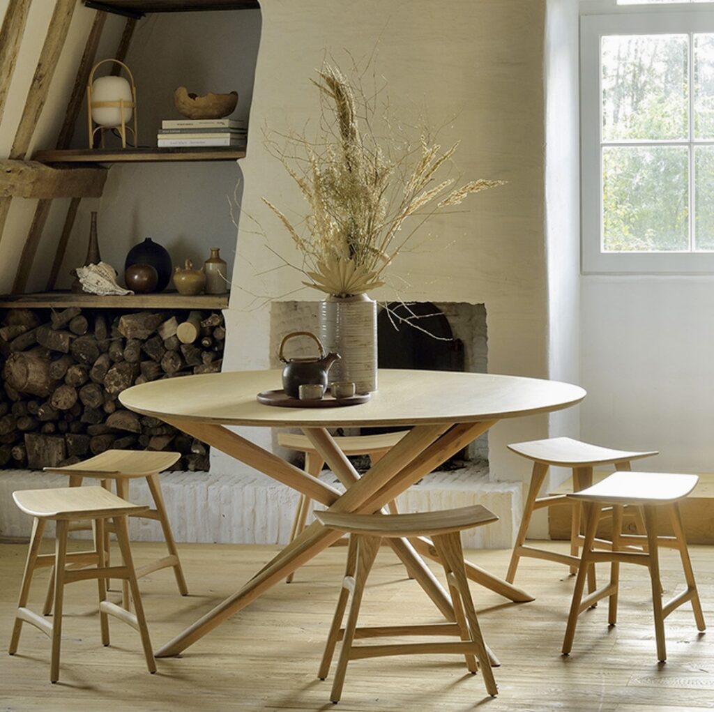Contemporary round dining table with sculptural wooden base, the Ethnicraft Mikado round dining table styled in a rustic interior with matching stools, natural oak tones, and soft neutral decor.