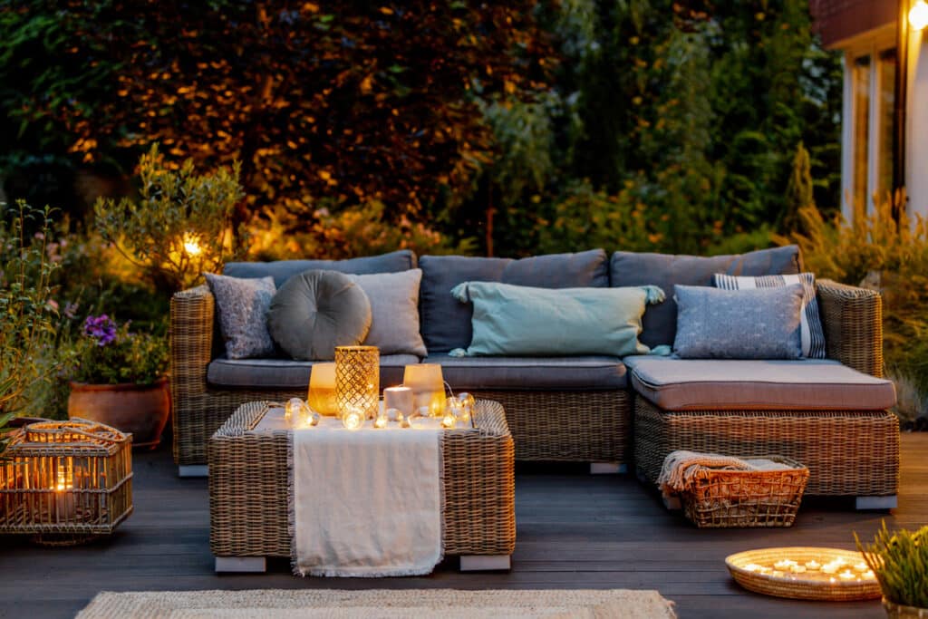 Woven corner garden sofa styled with cushions, lanterns, and candlelight for a cosy evening outdoor seating area