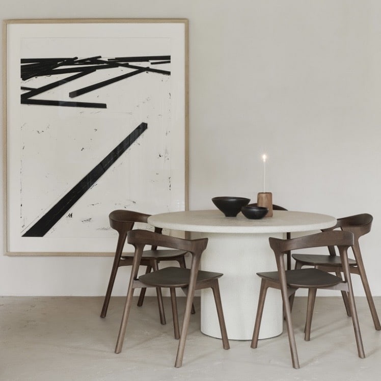 Pedestal Round dining table in pale micro cement stone finish with wooden dining chairs in a minimalist dining room