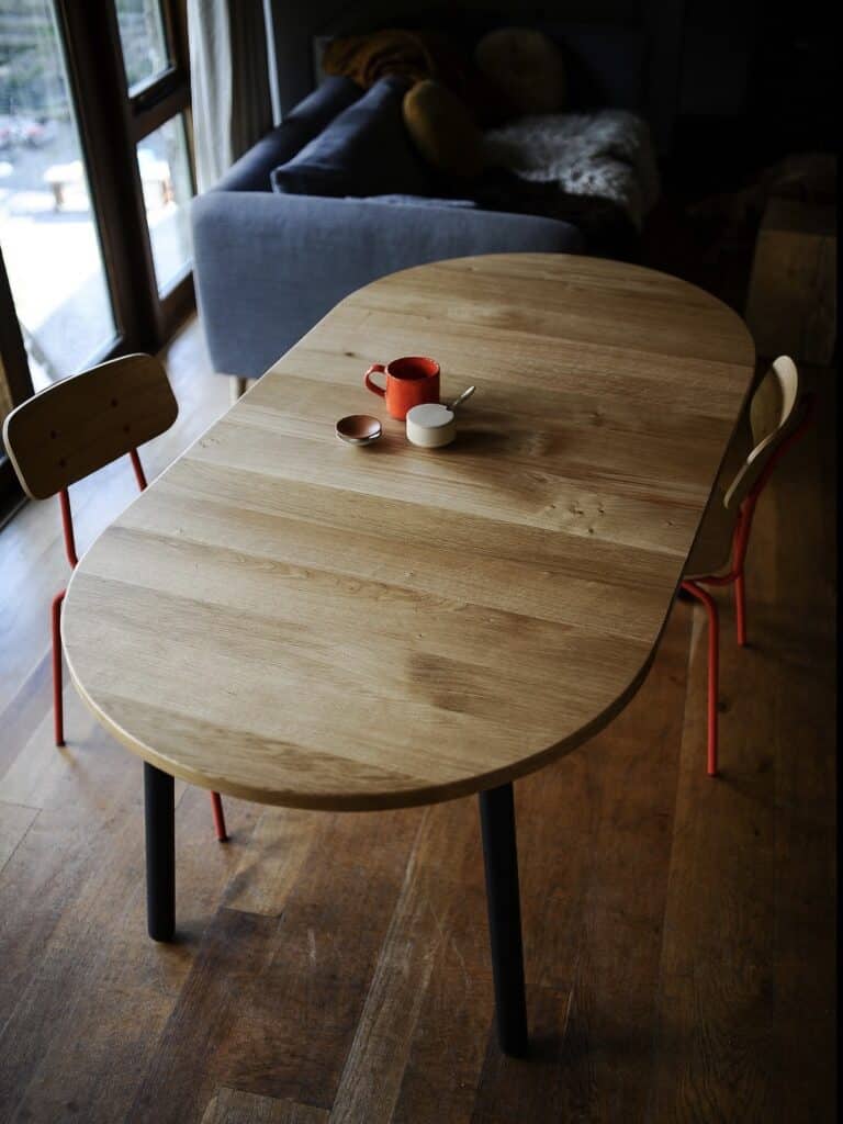 Affordable extendable solid oak dining table shown open in an oval shape with black legs