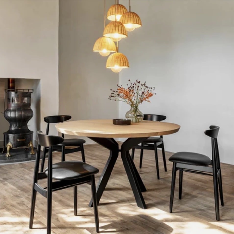 Modern pedestal round dining table with light wood top and black sculptural base in a contemporary dining room