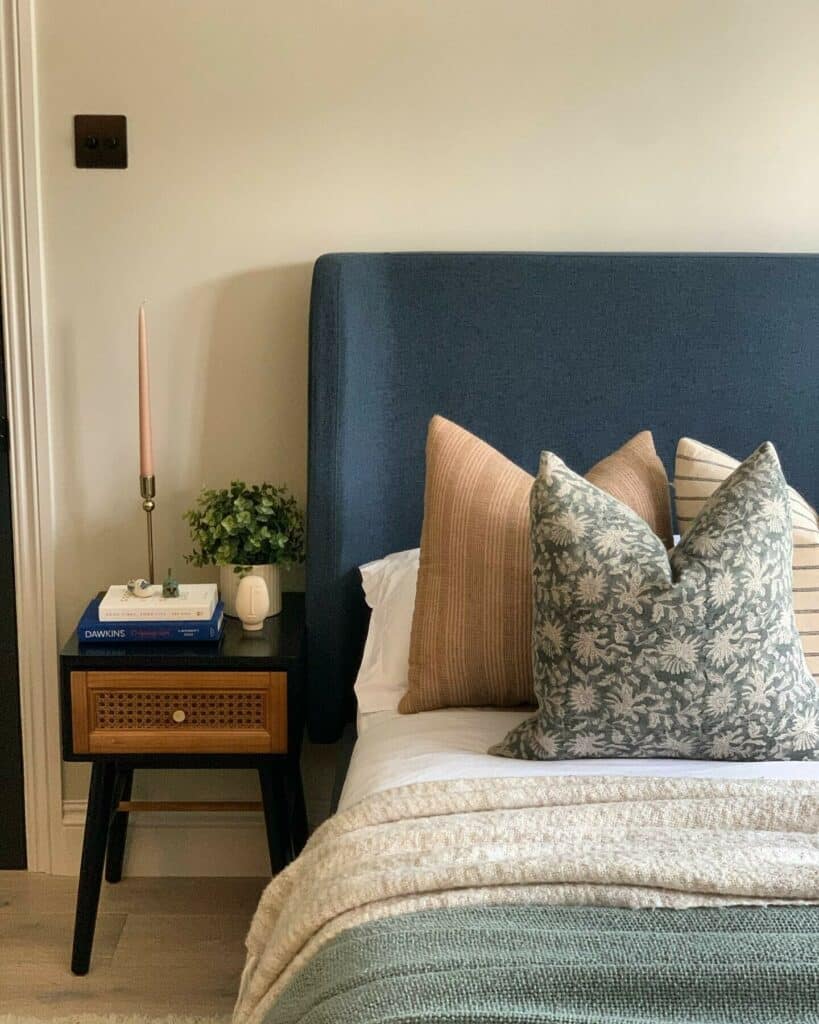 Blue and beige bedroom with navy upholstered headboard, Shaded White walls and layered floral and terracotta cushions