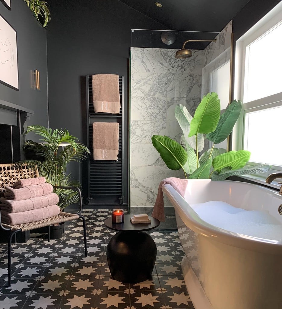 Black and white bathroom with black walls, marble shower, patterned star tile floor and pink towels