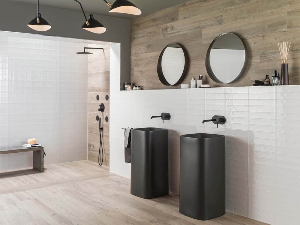 Black and white bathroom with Porcelanosa Manhattan Colonial wood-effect tile floor and wall, matte black pedestal basins, wall-mounted taps and round mirrors