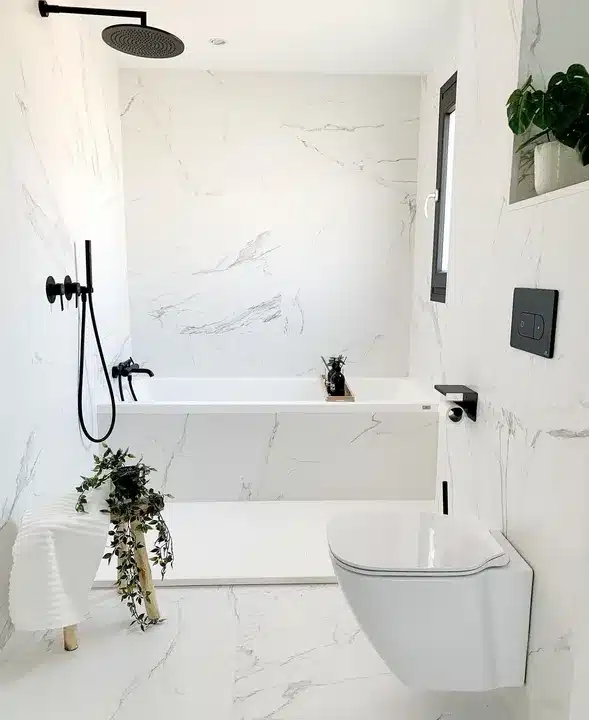 Small black and white bathroom with marble tile, freestanding bath and window bench