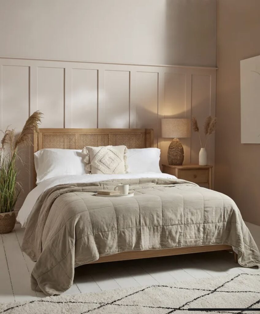 Beige bedroom featuring the Mia Bed from Cox & Cox with a woven rattan headboard, styled with soft beige bedding, pampas grass accents, and warm lighting for a chic boho look.