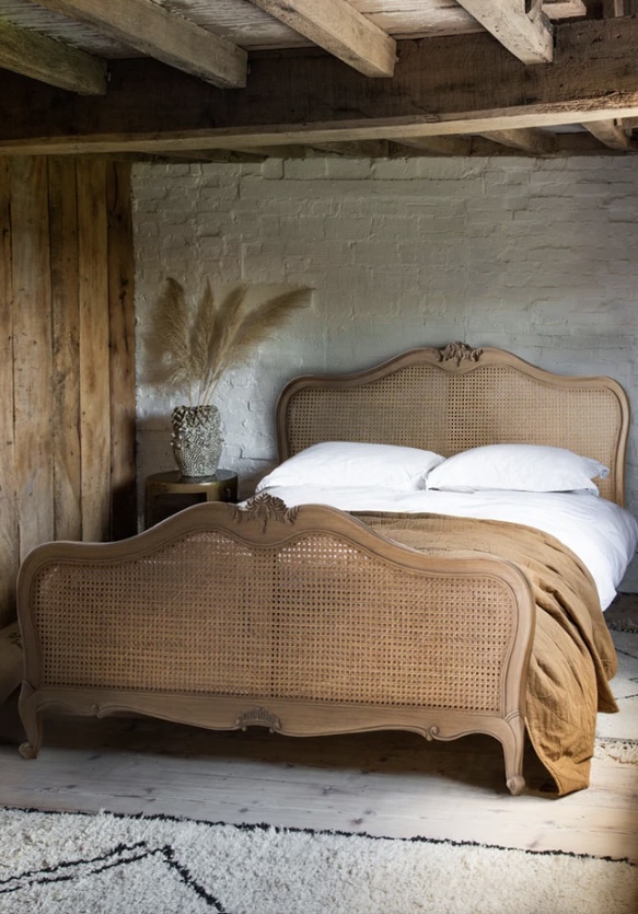 Antique-style wooden bedframe with cane panels styled in a rustic setting, showcasing beige bedroom ideas with natural textures and layered neutral tones.