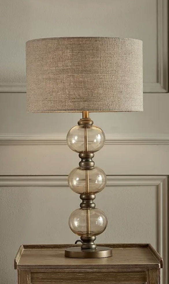 Aged bubble glass table lamp with a linen shade, adding warm ambient lighting and a sculptural touch to beige bedroom decor.