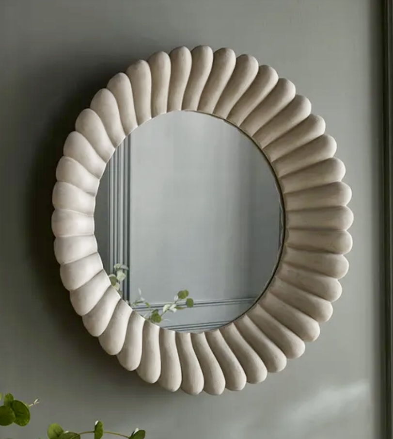 Round grey scalloped mirror with sculptural detailing, featured above the bed as part of a calming beige bedroom décor look.