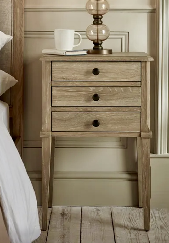 Rustic wood Myla Bedside Table with three drawers, styled in a beige bedroom décor setting beside the upholstered Myla bed.