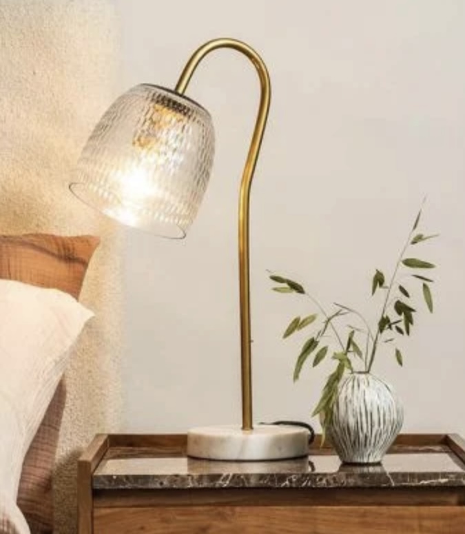 Brass and glass bedside table lamp with marble base, adding sculptural lighting and metallic accents to beige bedroom decor.