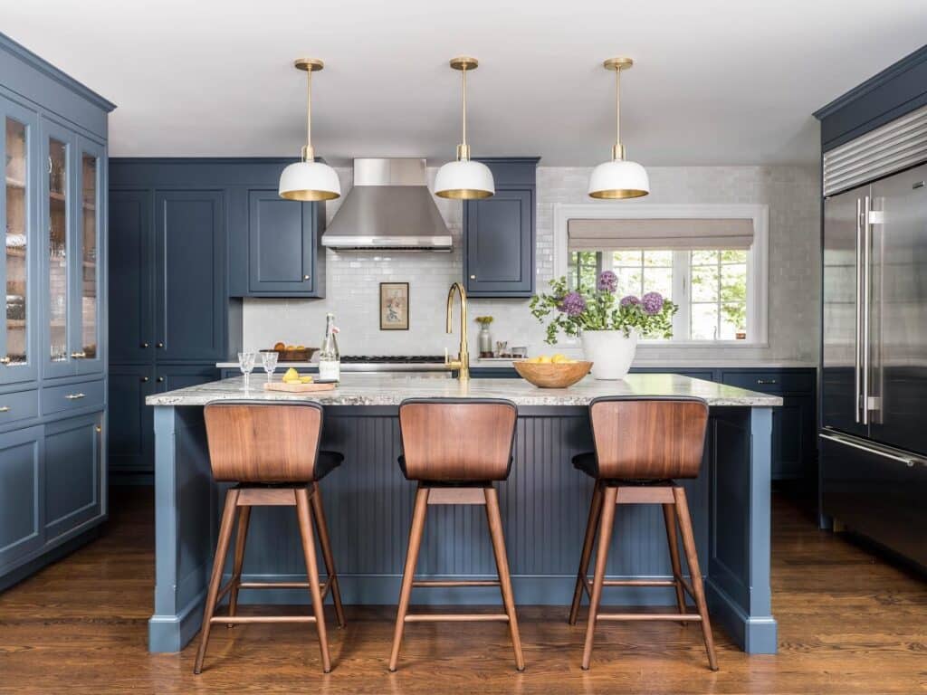 Hague Blue kitchen cabinets with marble worktop and island, walnut mid-century bar stools, brass pendant lights and glass-fronted display cabinets