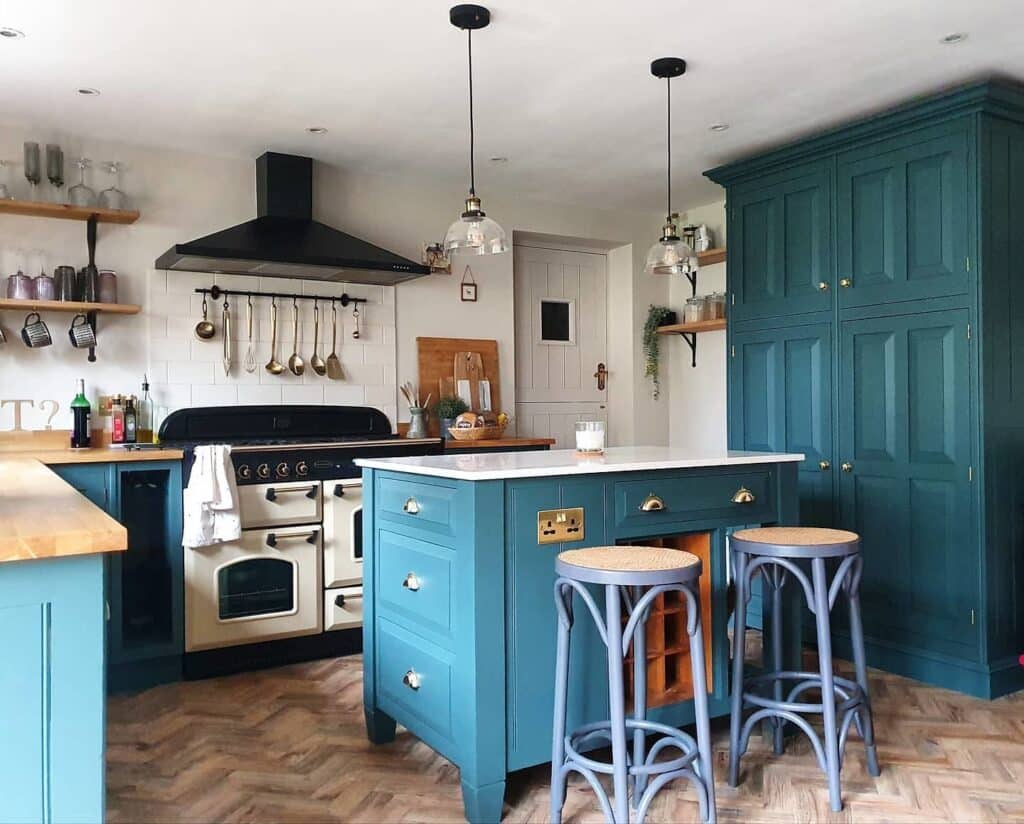 Inchyra Blue kitchen with cream range cooker, brass cup handles, rattan bar stools, freestanding kitchen island with wine rack and herringbone reclaimed wood floor.​​​​​​​​​​​​​​​​