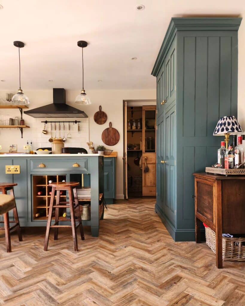 Inchyra Blue full-height shaker pantry cupboard with brass hardware, freestanding kitchen island with wine rack and herringbone reclaimed wood flooring.