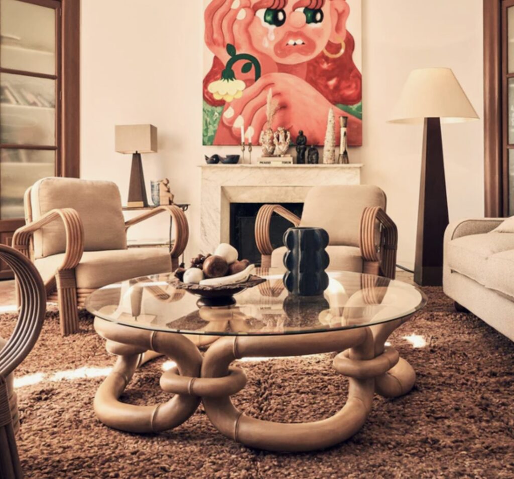 Contemporary living room featuring a sculptural glass top coffee table with bamboo-inspired base, styled with neutral furnishings and bold wall art.