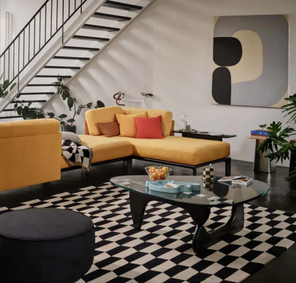 Bold modern living room with black base Vitra glass coffee table, glass top coffee table on black and white patterned rug and yellow sofa.