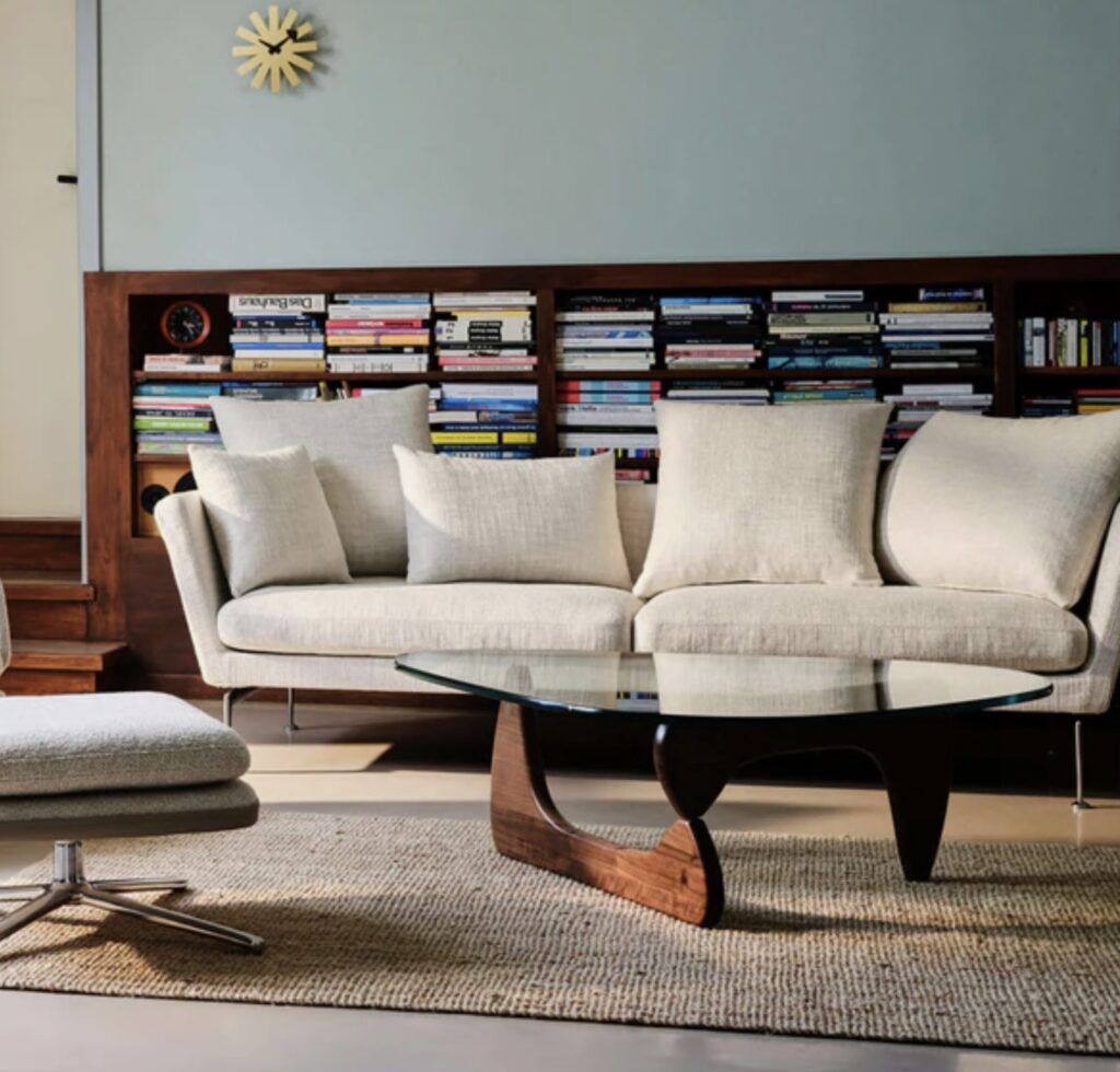Neutral living room with cream sofa and Vitra glass coffee table featuring a walnut base and curved glass top coffee table design.
