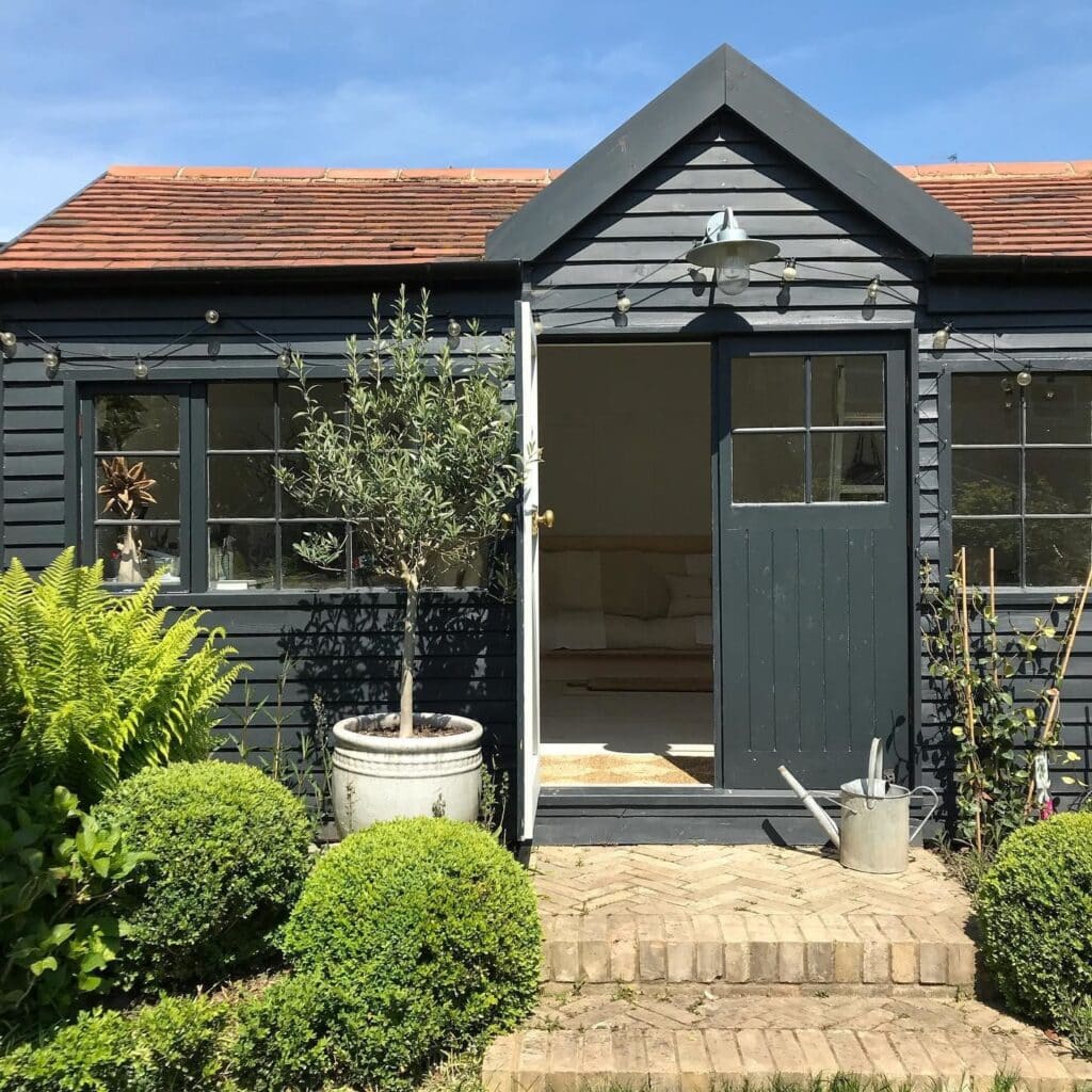 Off-Black painted garden summerhouse with weatherboard cladding and festoon lights