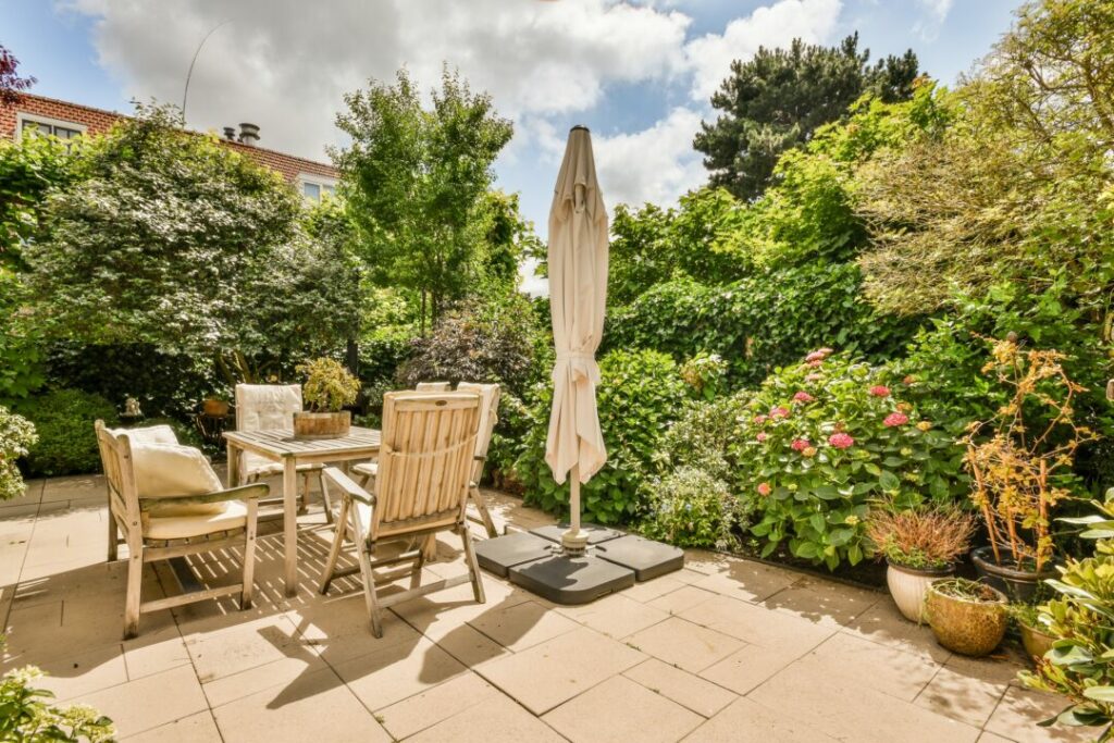 Charming courtyard garden with a wooden outdoor dining set, lush greenery, and a sun umbrella. A beautiful and inviting example of courtyard garden ideas for alfresco dining and relaxation.